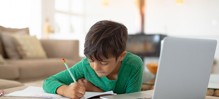 A school-aged boy is working on a lesson at his computer in his home.