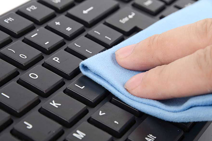 Woman cleaning computer keyboard using disinfection wipes.