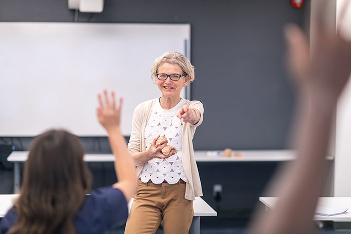 A professor in a classroom calling on a student raising their hand.