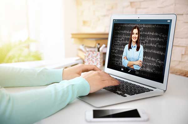 Laptop with hands at the keyboard. On the screen is a teacher at another location.