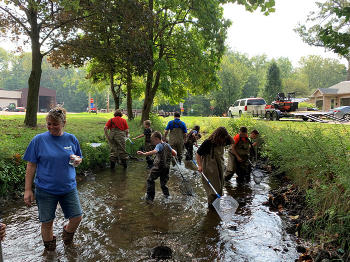 Da-Lite volunteers and students in waders are exploring a stream.