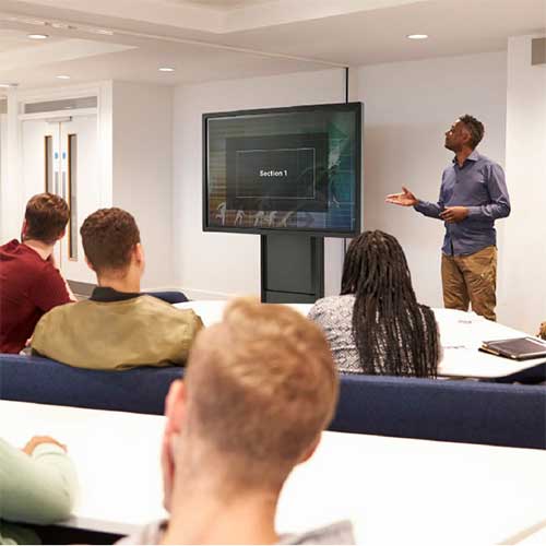 Classroom with instructor next to display on a cart.