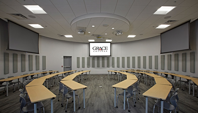 Classroom with rows of tables facing each other and projection screens at each end.