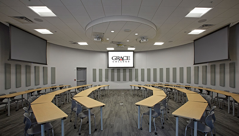 Classroom with rows of tables facing each other and projection screens at each end.
