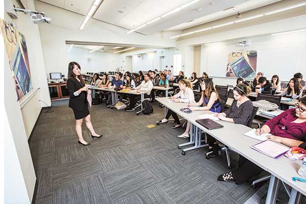 Instructor standing in front of classroom with IDEA screen surface. Students taking notes.