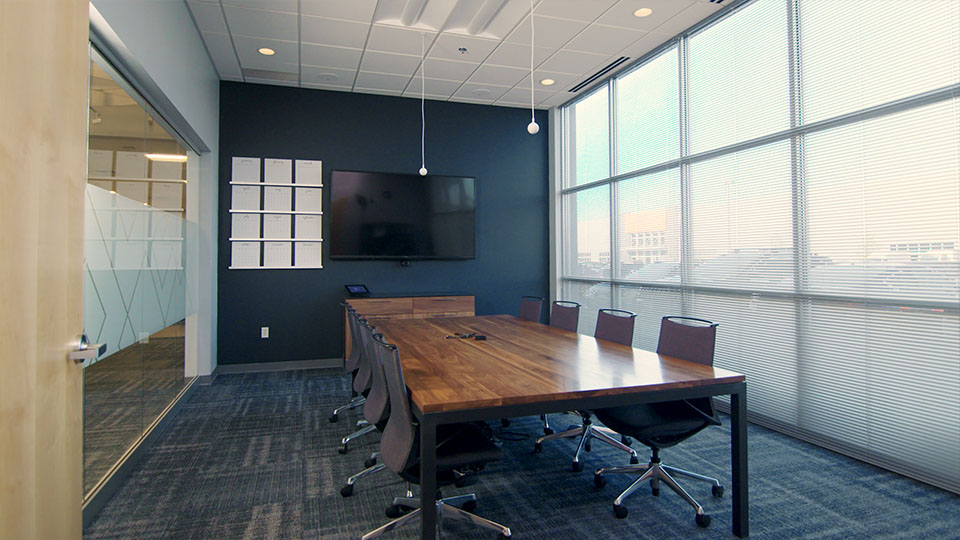 board room with floor-to-ceiling windows, brown wood table, black chairs and Vaddio conferencing camera and set of two ceiling microphones
