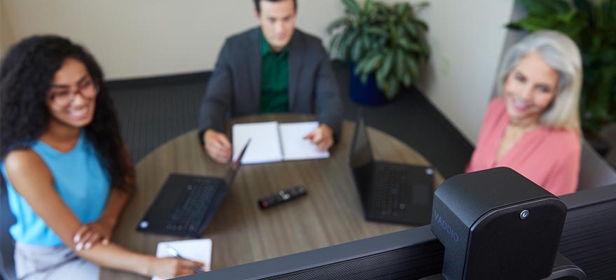 ConferenceSHOT ePTZ mounted above display, three people sitting around table in huddle room