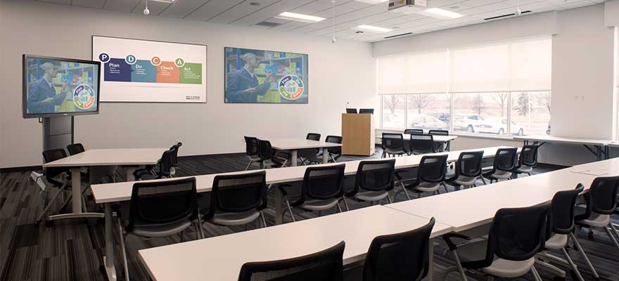 Large room with desks and chairs with a lectern, display cart, projector screens, projector mounts, camera tracking and ceiling microphones.